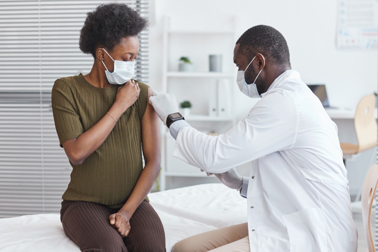 African doctor in white coat vaccinating pregnant woman during her visit at hospital