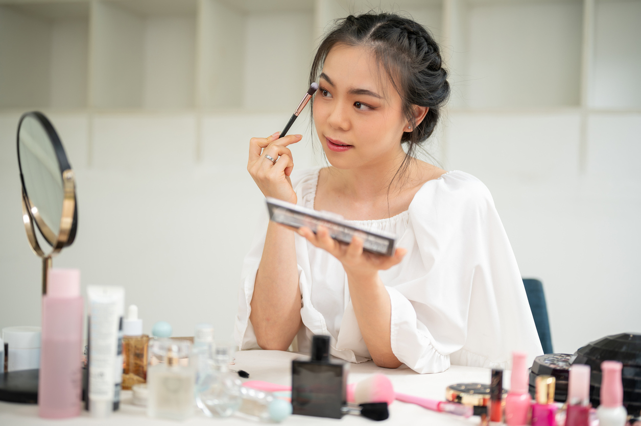 <p>Young woman applying mascara to her eyelashes, using drugstore makeup brands</p>