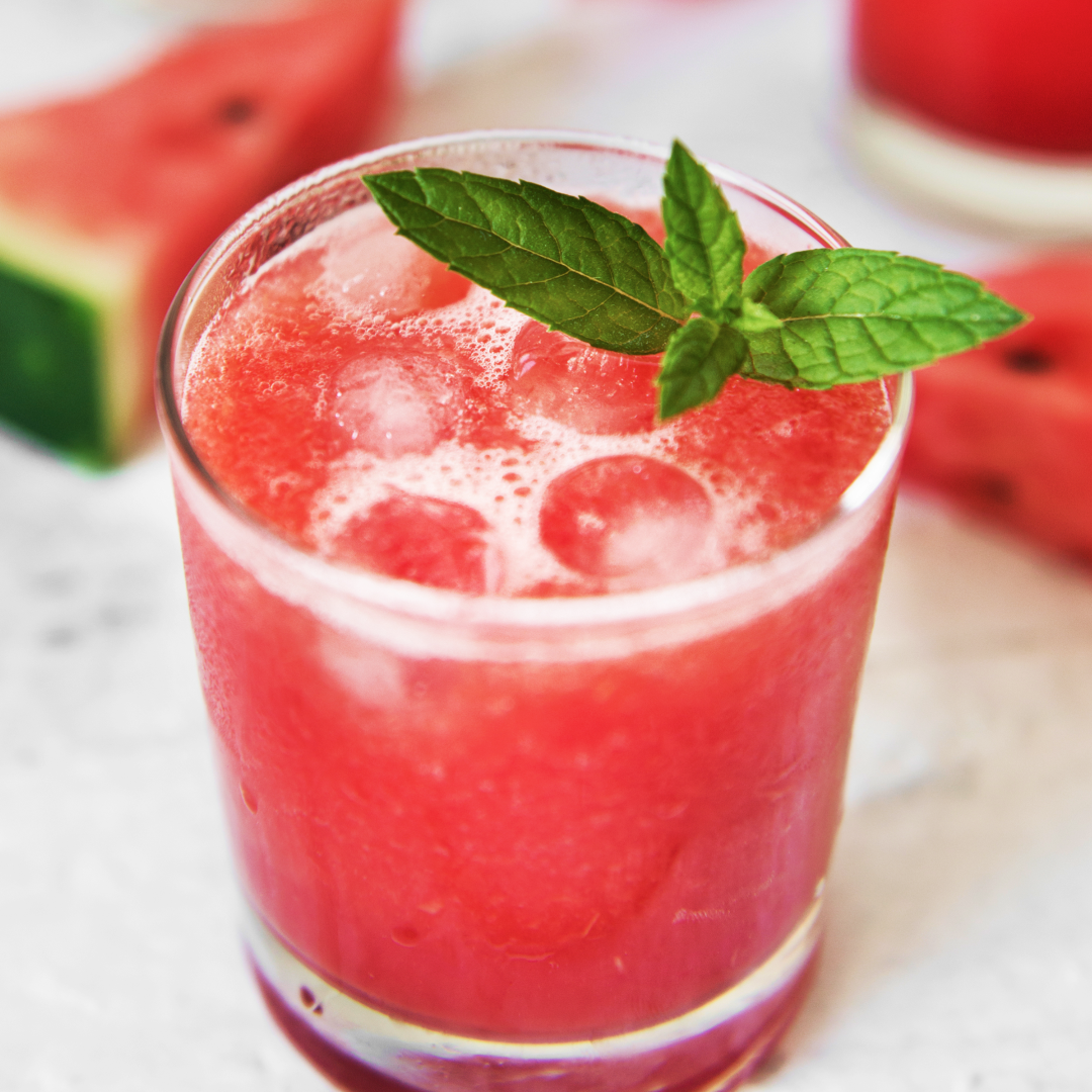 <p>Two watermelon mint julep drinks on a table in front of a plate of watermelon slices</p>
