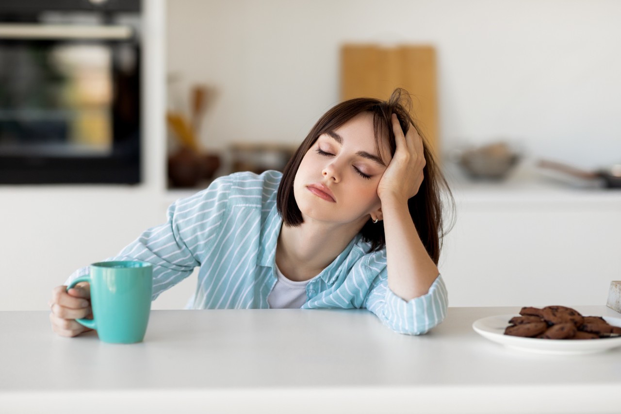 Tired woman leans on kitchen counter with cup of coffee
