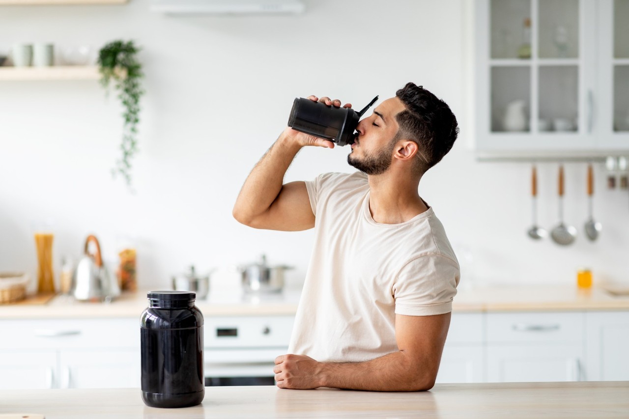 Young man drinking a fitness beverage in his kitchen.
